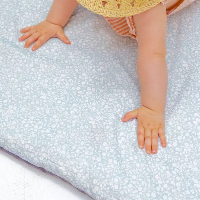 Les mains d'un bébé posées à plat sur un tapis d'éveil bleu pâle imprimé de petites fleurs blanches