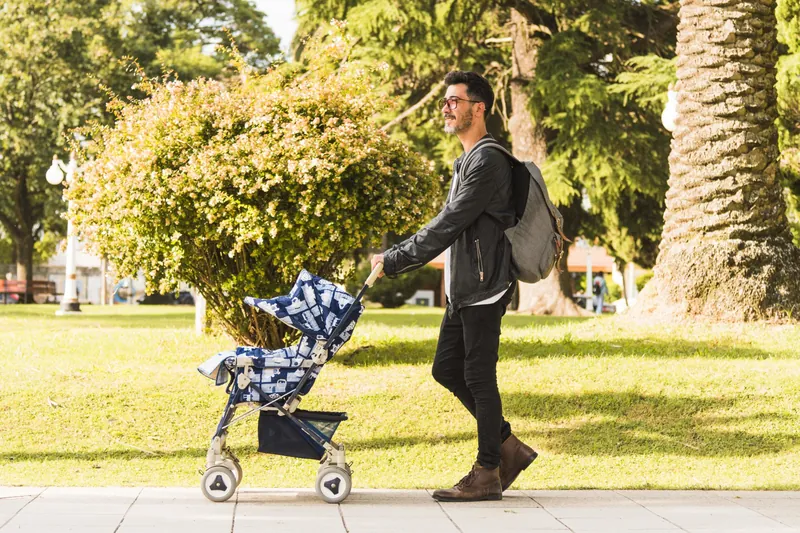Un homme qui pousse une poussette pliable dans un parc ensoleillé