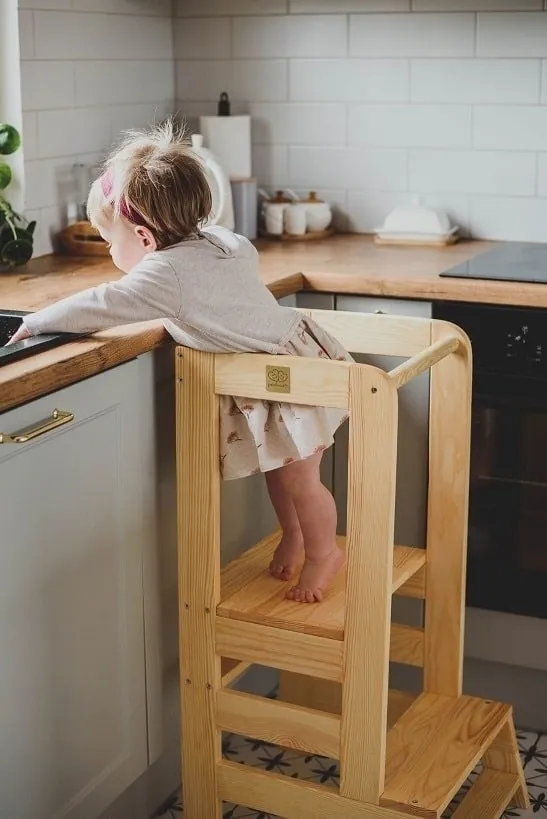 Une petite fille debout sur une tour d'observation en bois, penchée sur le plan de travail d'une cuisine