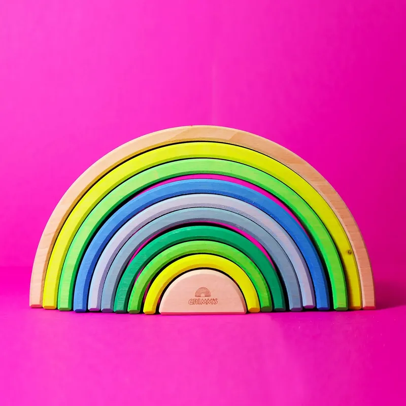 Un arc-en-ciel en bois à empiler, aux arches de couleurs vives, sur fond rose fuchsia