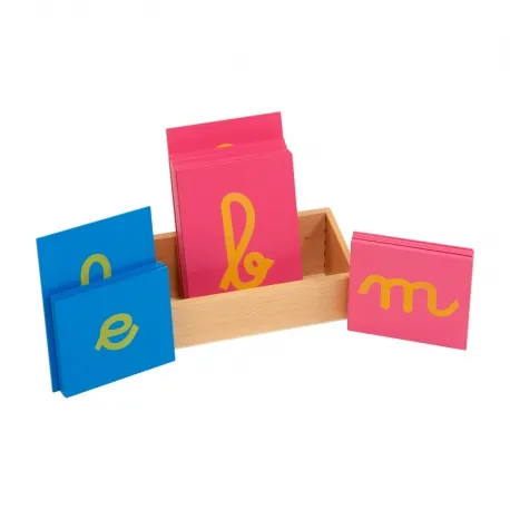 Des lettres rugueuses Montessori, cursives vertes et jaunes sur des plaquettes bleues et roses, rangées dans une boîte en bois