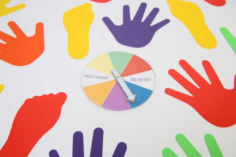 Des empreintes de mains et de pieds de couleur posées au sol autour d'une roue des couleurs à flèche