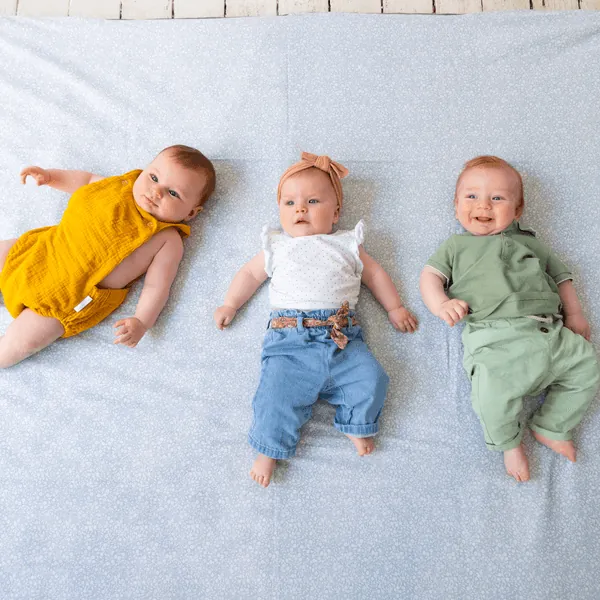 Trois bébés allongés côte à côte sur le dos, sur un tapis d'éveil bleu ciel