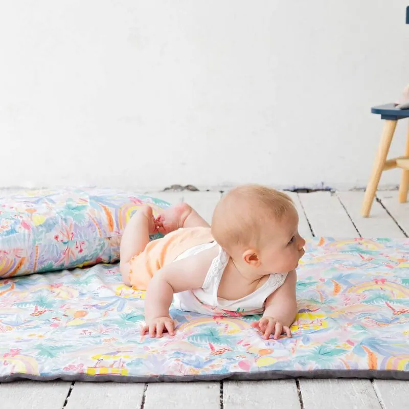 Un bébé à plat ventre sur un tapis d'éveil imprimé, posé sur un parquet blanc, qui regarde sur le côté