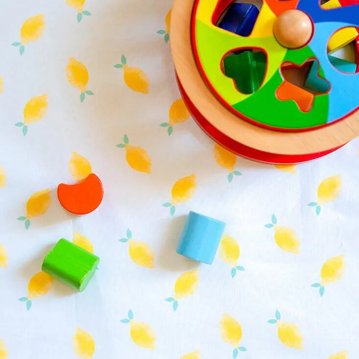 Une boîte à formes en bois et des blocs de couleur posés sur un tissu imprimé de citrons
