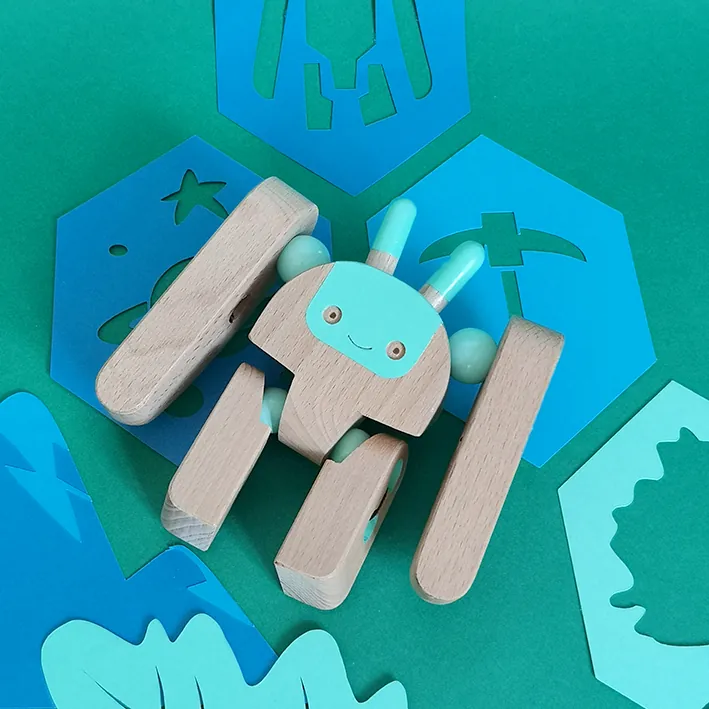 Une figurine de robot en bois articulée, au visage bleu, posée sur des formes découpées bleues et vertes