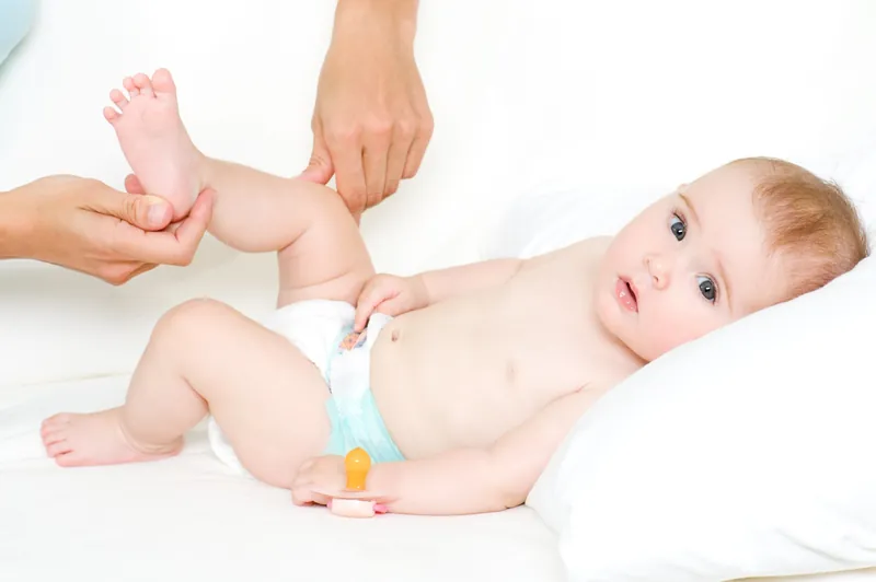 Un bébé en couche allongé sur un oreiller blanc pendant qu'un adulte lui tient la jambe