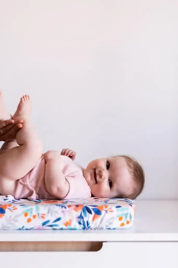 Un bébé souriant allongé sur le côté, sur un matelas à langer imprimé de fleurs posé sur une commode blanche