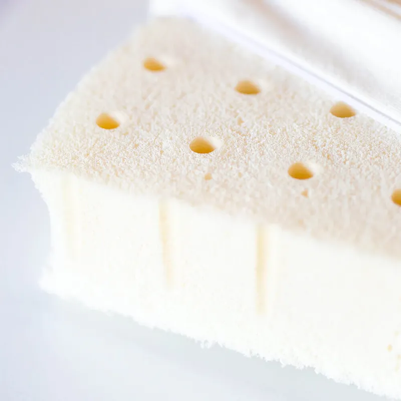 Un bloc de mousse en latex naturel blanc crème, percé de petits trous, vu en gros plan