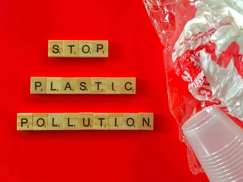 Des lettres de Scrabble qui forment « Stop plastic pollution » sur un fond rouge, à côté d'un sac et de gobelets en plastique