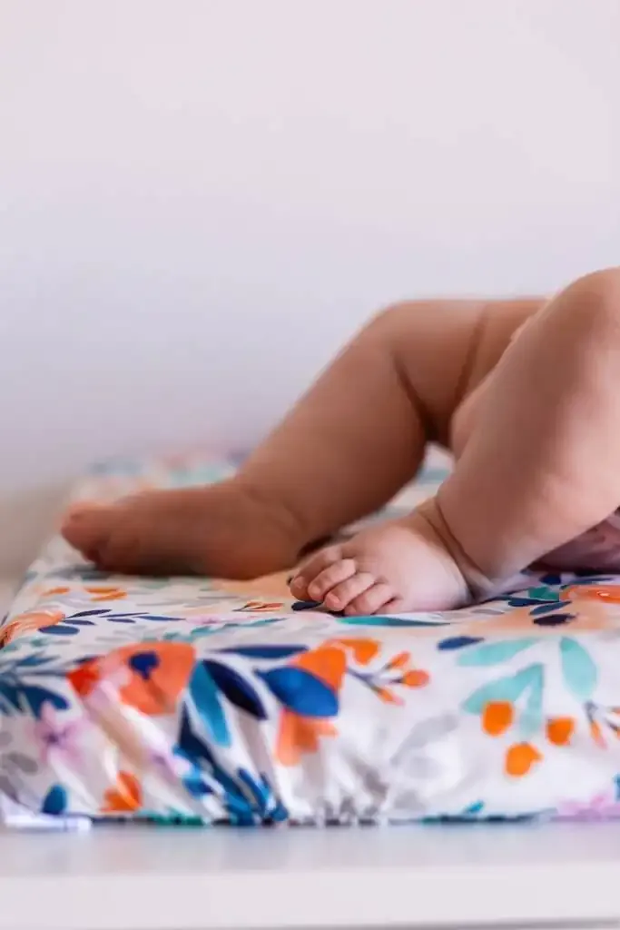 Les jambes d'un bébé posées sur un matelas à langer imprimé de grosses fleurs orange et bleues