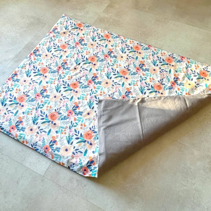 Un tapis d'éveil imprimé de fleurs posé sur un carrelage, un coin replié qui montre sa face grise