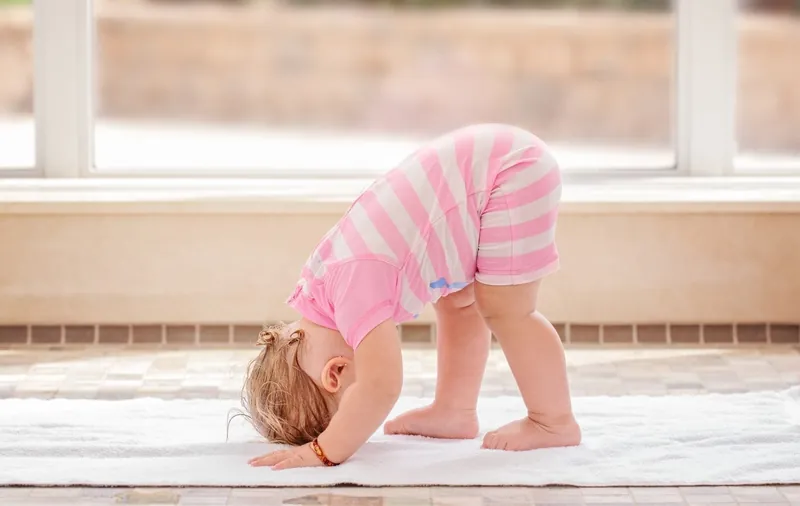 Un bébé en body rayé rose, debout sur une serviette, les mains et la tête au sol, jambes tendues