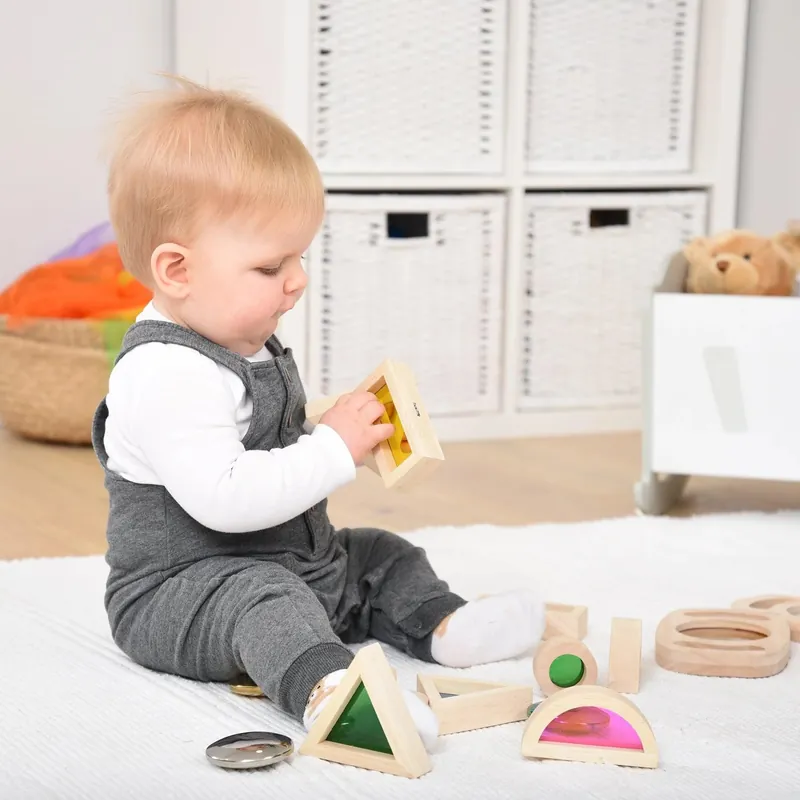 Un bébé assis sur un tapis blanc qui manipule des blocs sensoriels en bois à fenêtres colorées