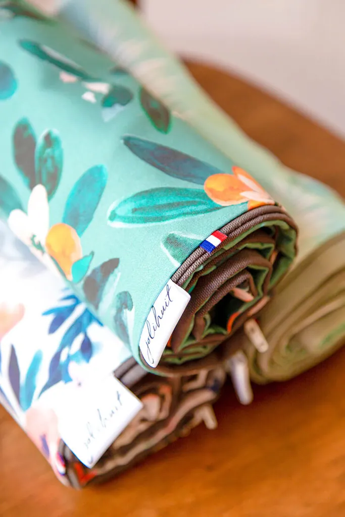 Des housses de tapis imprimées, roulées et empilées sur une table en bois, avec l'étiquette Jolihuit et un petit drapeau français