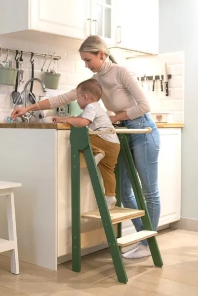 Une maman et son petit garçon debout sur une tour d'observation en bois vert, qui lavent des légumes à l'évier de la cuisine