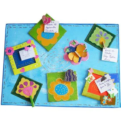 Une page de scrapbooking sur fond bleu, décorée de fleurs en carton, de cadres colorés et de petites étiquettes écrites à la main