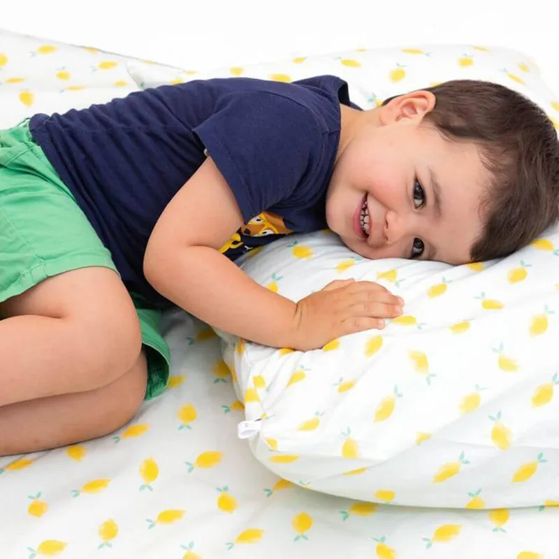 Un petit garçon souriant allongé sur un oreiller blanc imprimé de citrons jaunes