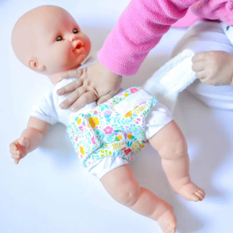 Des mains d'enfant qui mettent une couche en tissu fleuri à un poupon allongé