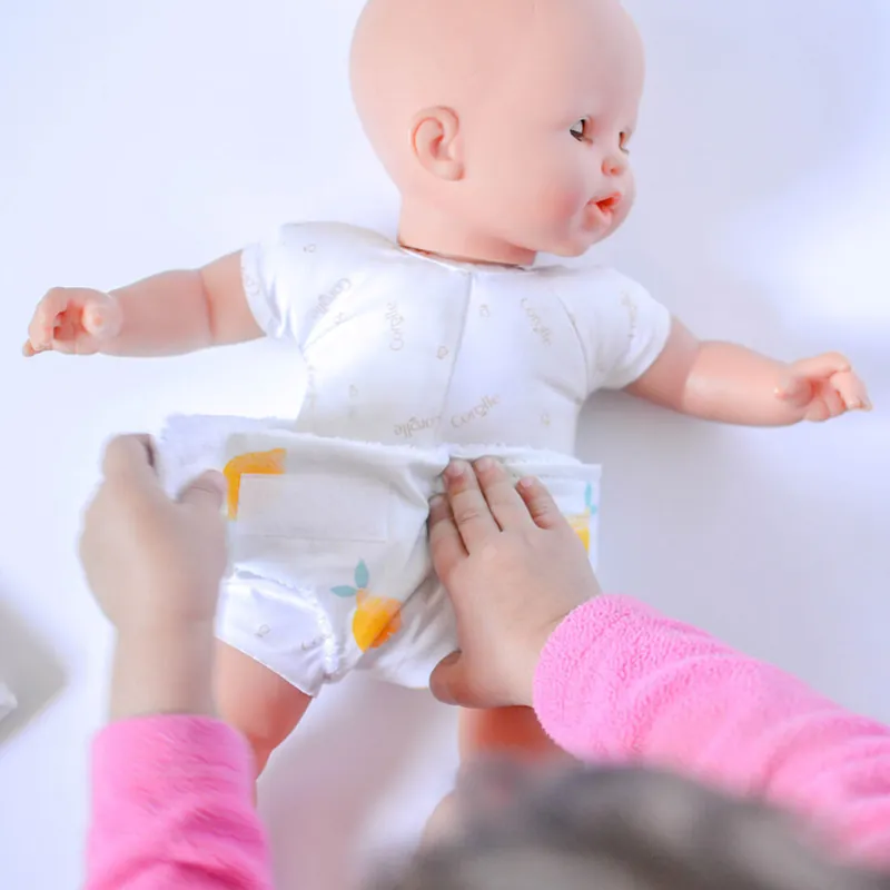 Des mains d'enfant qui attachent une couche blanche imprimée de citrons sur un poupon