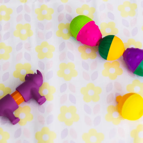 Gros plan sur des jouets à emboîter colorés et un petit marteau violet, posés sur un tapis d'éveil imprimé de fleurs jaunes et lilas