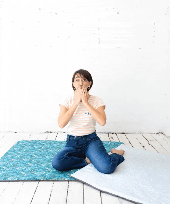 Aude, la fondatrice de Jolihuit, assise en tailleur sur un tapis d'éveil bleu, les mains sur la bouche d'un air ravi