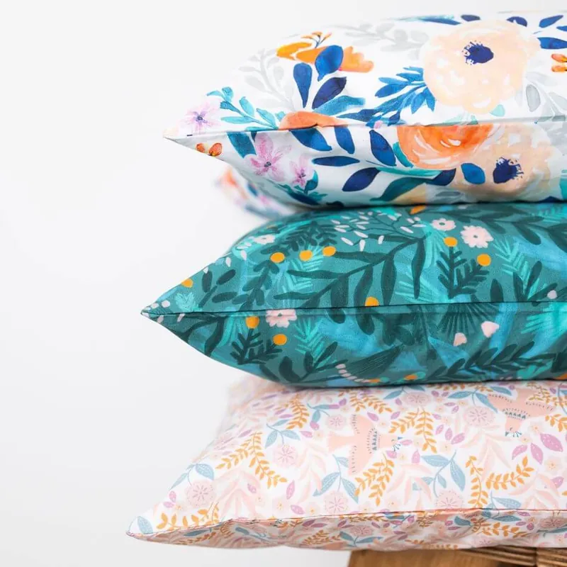 Trois oreillers empilés aux housses imprimées de fleurs : bleu et orange sur fond blanc, feuillages sur fond vert canard, petites fleurs sur fond rose pâle