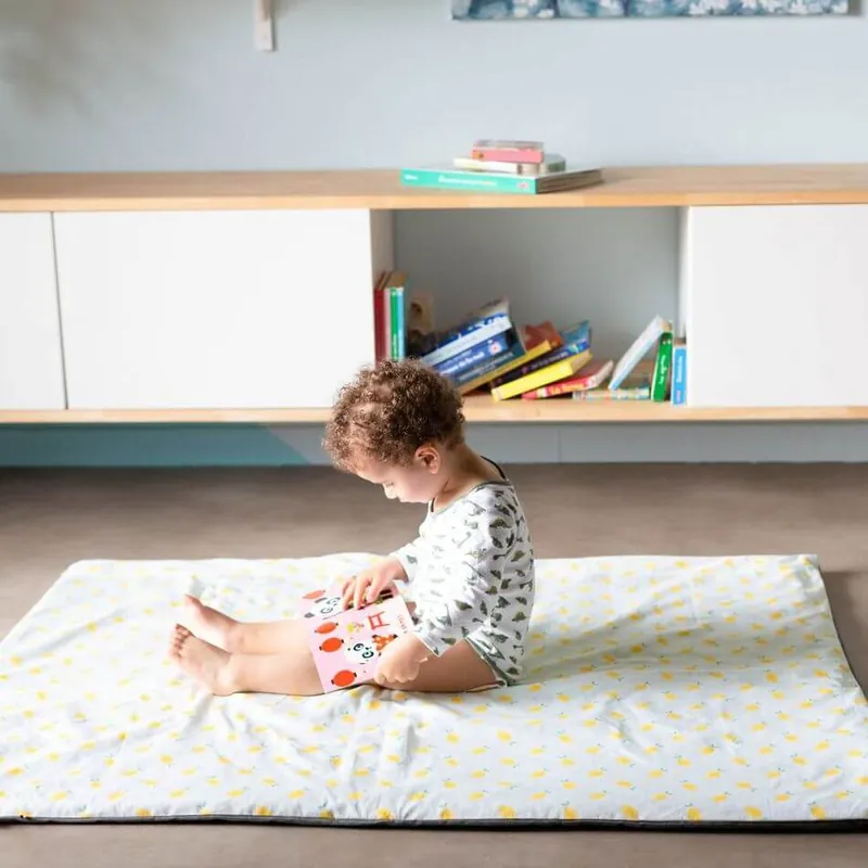 Un enfant assis sur un grand tapis d'éveil blanc imprimé de citrons, un livre ouvert sur les genoux