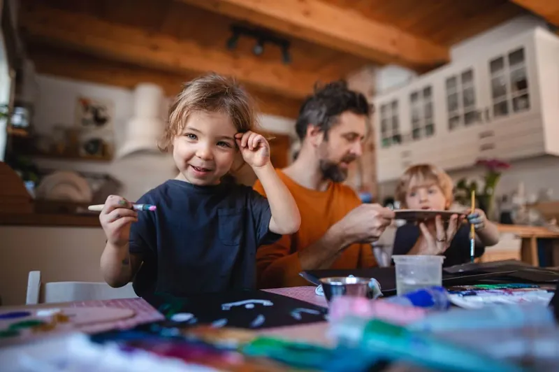 Une petite fille et un petit garçon dessinent et peignent à une table avec leur père, dans une cuisine