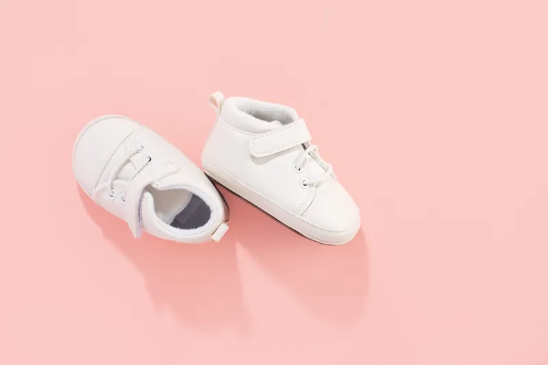 Une paire de petits chaussons de bébé blancs à scratch sur un fond rose