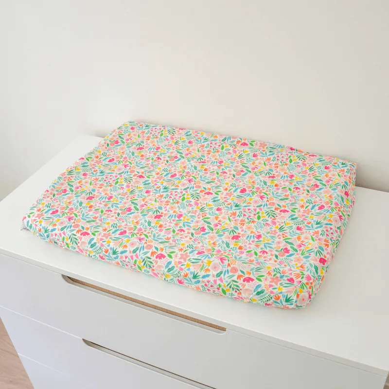 Un matelas à langer à housse imprimée de petites fleurs multicolores, posé sur une commode blanche