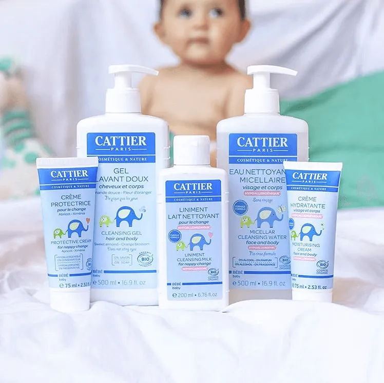 La gamme bébé Cattier : crème protectrice, gel lavant doux, liniment, eau nettoyante micellaire et crème hydratante, devant un bébé