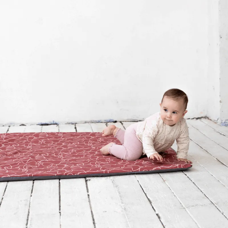 Bébé à quatre pattes sur un tapis d'éveil rouge à motifs blancs, dans une pièce blanche au parquet peint