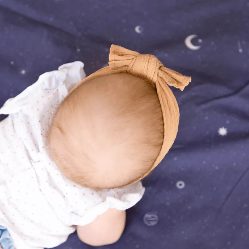 Bébé avec un bandeau noué couleur caramel, vu de dessus, allongé sur le ventre sur un tapis bleu nuit étoilé