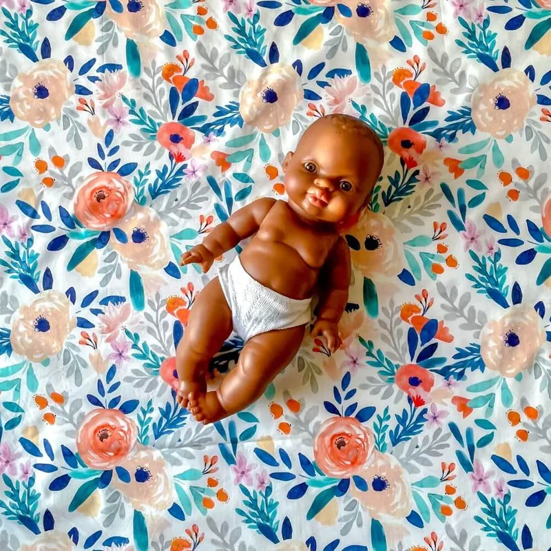 Vue de dessus d'un poupon en couche posé sur un tapis d'éveil à grandes fleurs pêche et bleues