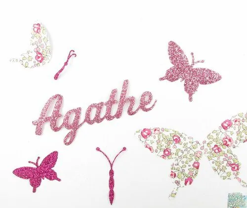 Le prénom « Agathe » en lettres à paillettes roses, entouré d'appliques thermocollantes en forme de papillons, en tissu fleuri et à paillettes