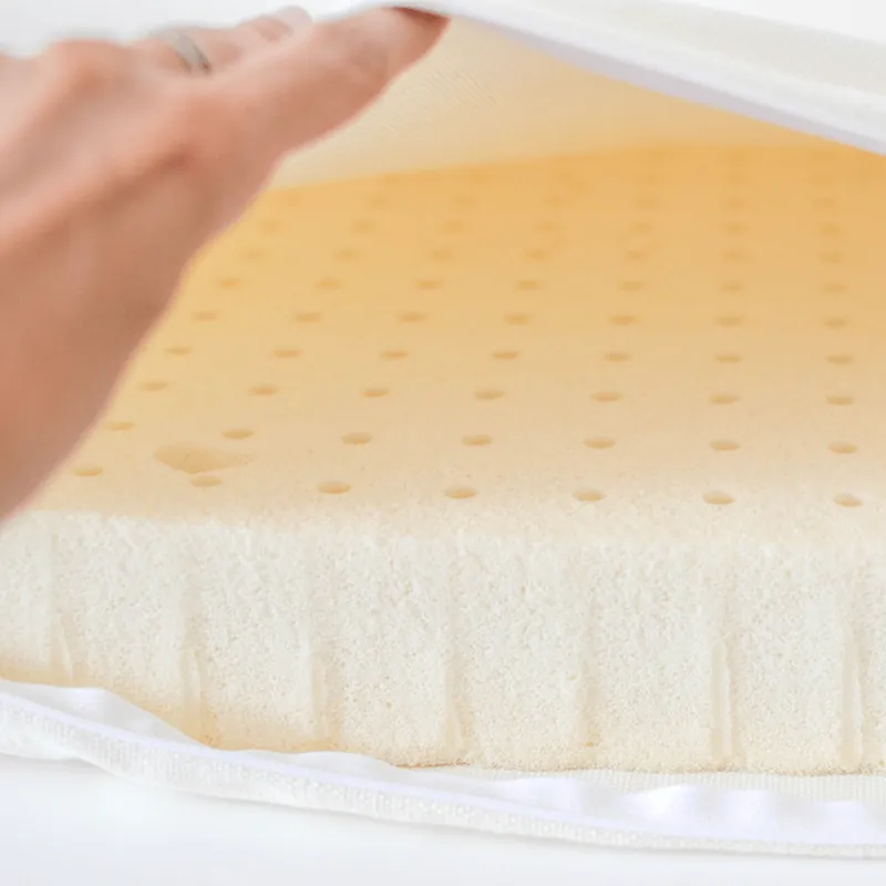 Une main soulève une housse blanche et découvre la mousse de latex naturel alvéolée, couleur crème