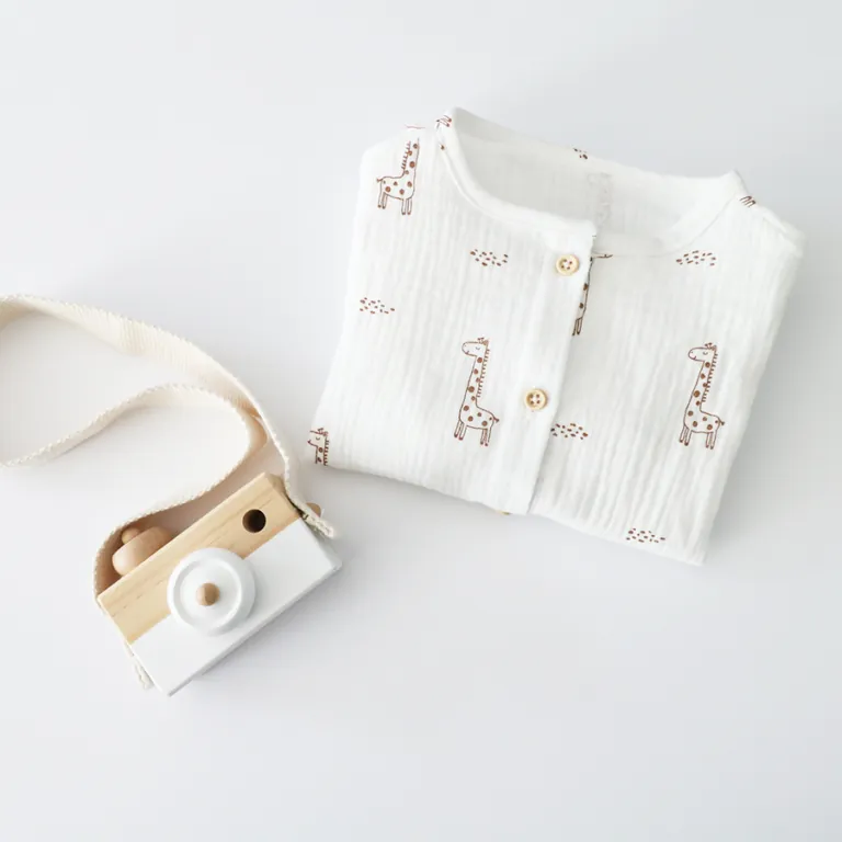 Chemise blanche à girafes pliée à côté d'un appareil photo en bois pour enfant