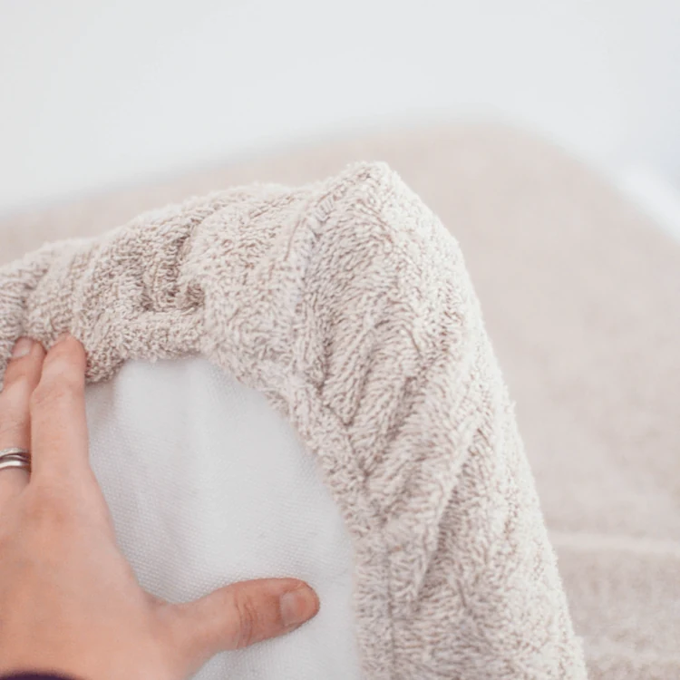 Une main retire l'éponge écrue du matelas à langer et découvre l'alèse blanche en dessous.