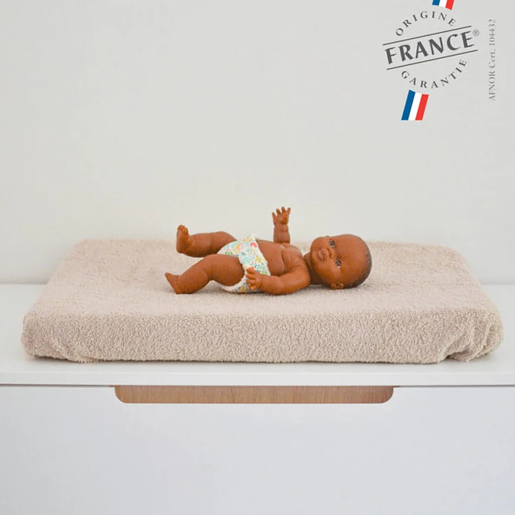 Le matelas à langer Jolihuit habillé de son éponge écrue, posé sur une commode blanche, un poupon dessus