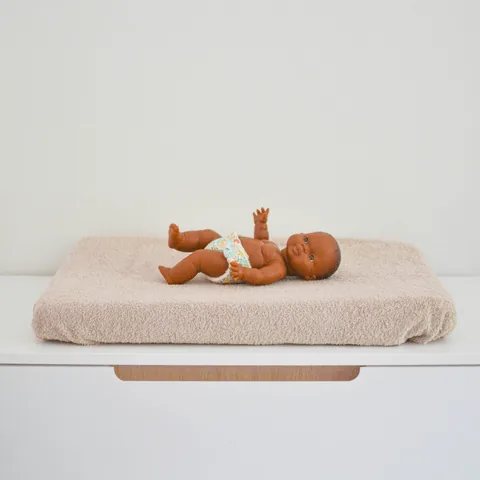 Poupon allongé sur le matelas à langer en housse éponge écrue, posé sur une commode blanche
