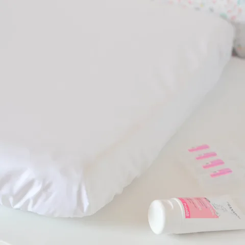 Angle de la housse imperméable blanche, tube de crème et dosettes posés à côté