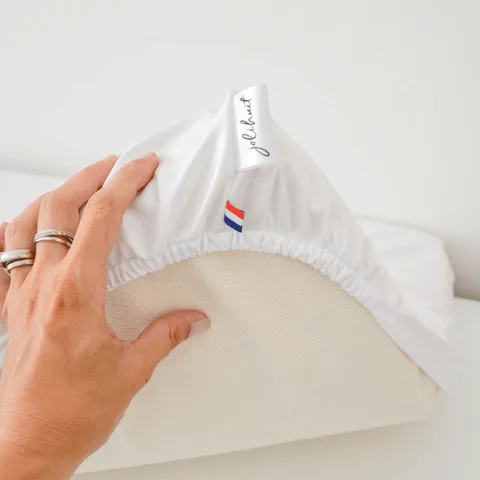 Main qui soulève l'angle élastiqué de la housse imperméable, étiquette Jolihuit et drapeau tricolore