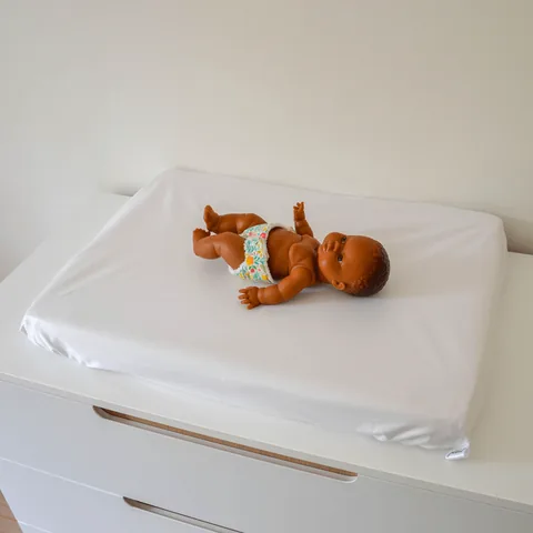 Poupon allongé sur le matelas à langer en housse imperméable blanche, posé sur une commode blanche