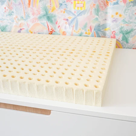 Un bloc de mousse de latex naturel couleur crème, percé de rangées de trous, posé nu sur une commode blanche