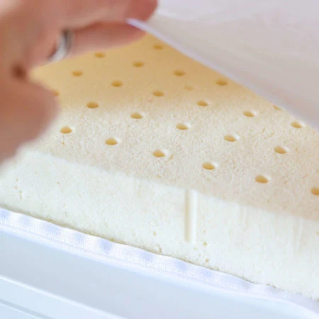 Une main soulève l'alèse écrue et découvre la mousse de latex perforée.
