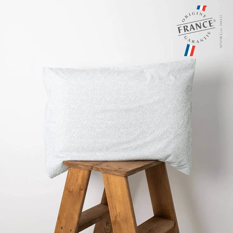 L'oreiller enfant Jolihuit posé sur un tabouret de bois, dans l'imprimé Gabi, un semis de petites fleurs blanches sur un vert d'eau très pâle