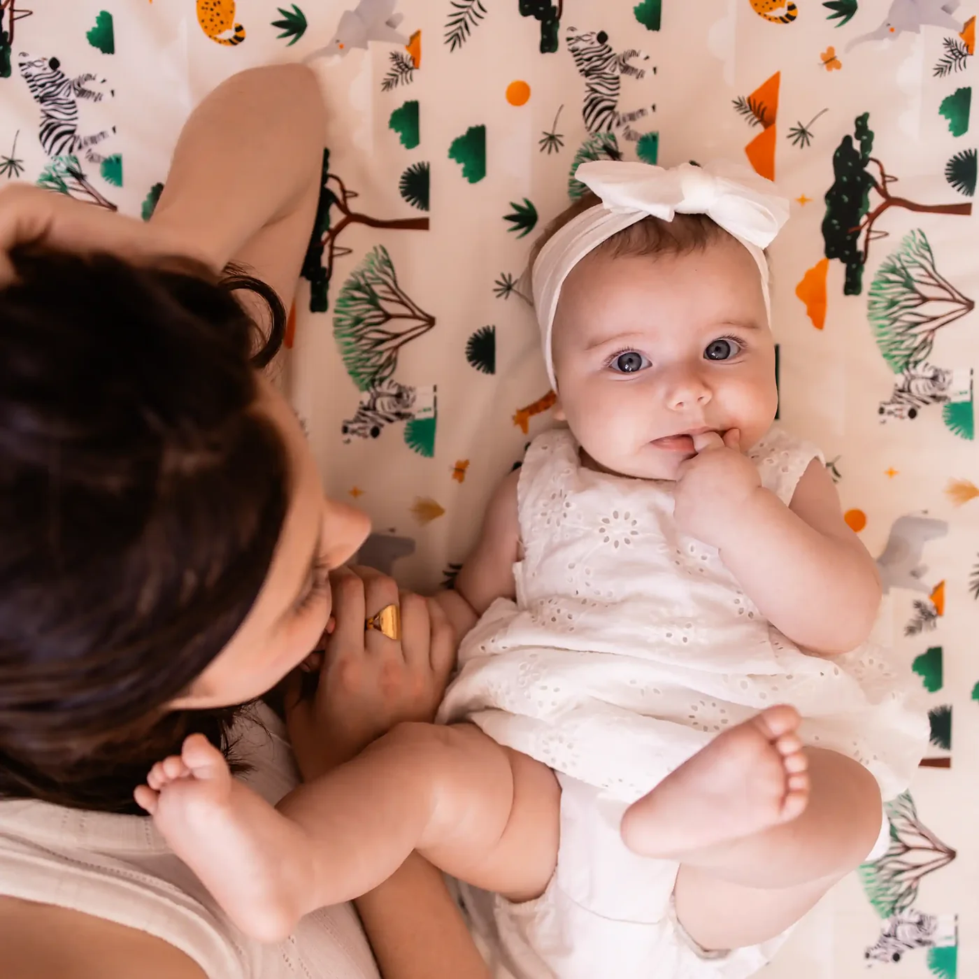 Sa mère penchée au-dessus d’elle, le bébé regarde l’objectif, allongé sur le tapis imprimé savane.