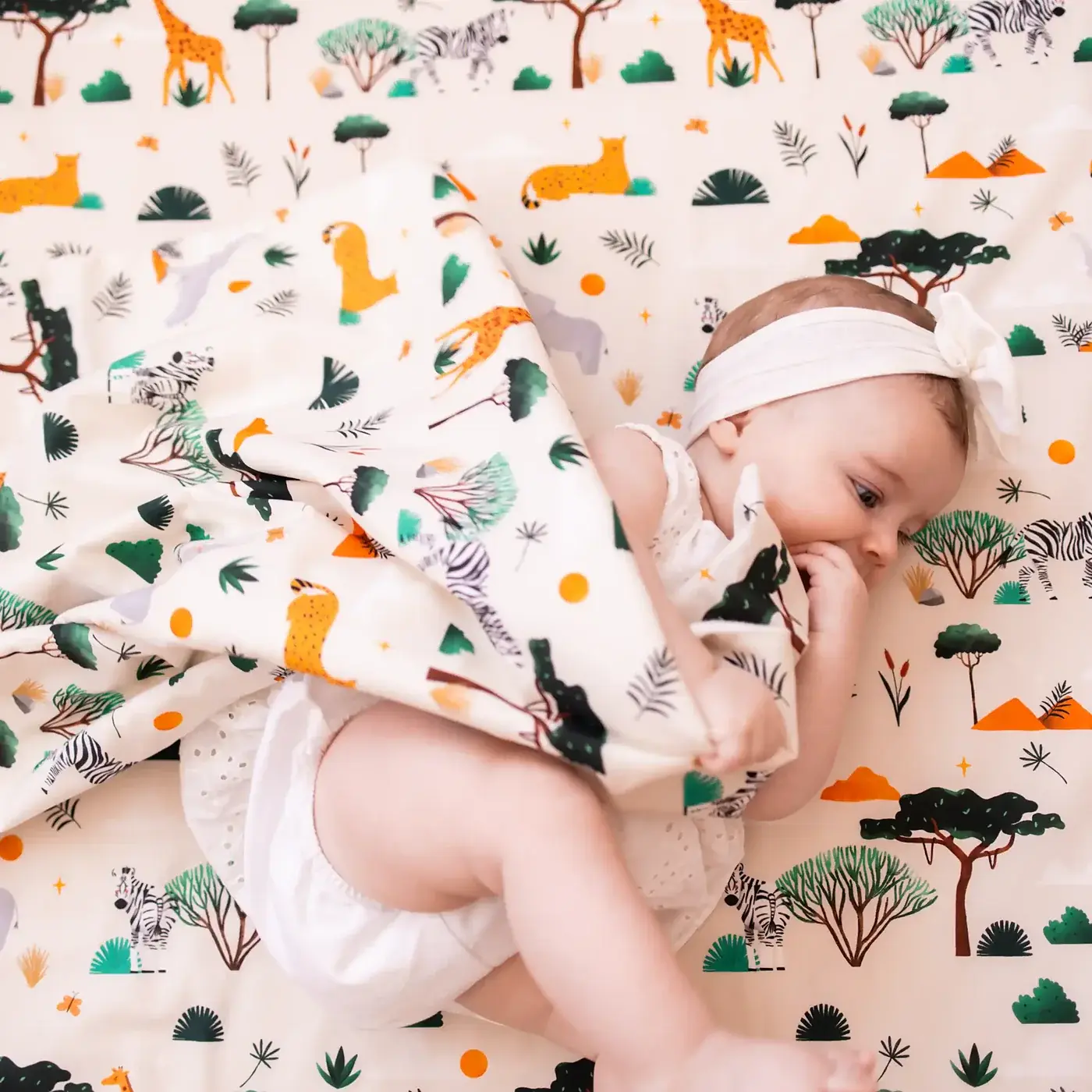 Le bébé attrape la housse imprimée savane et la ramène sur lui, vu de dessus.